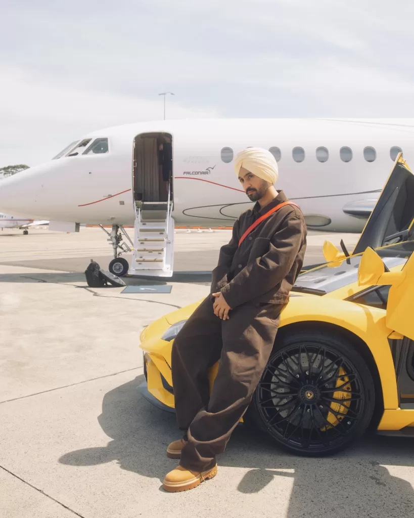 Diljit wearing brown colored clothes and standing in front of an airplane.