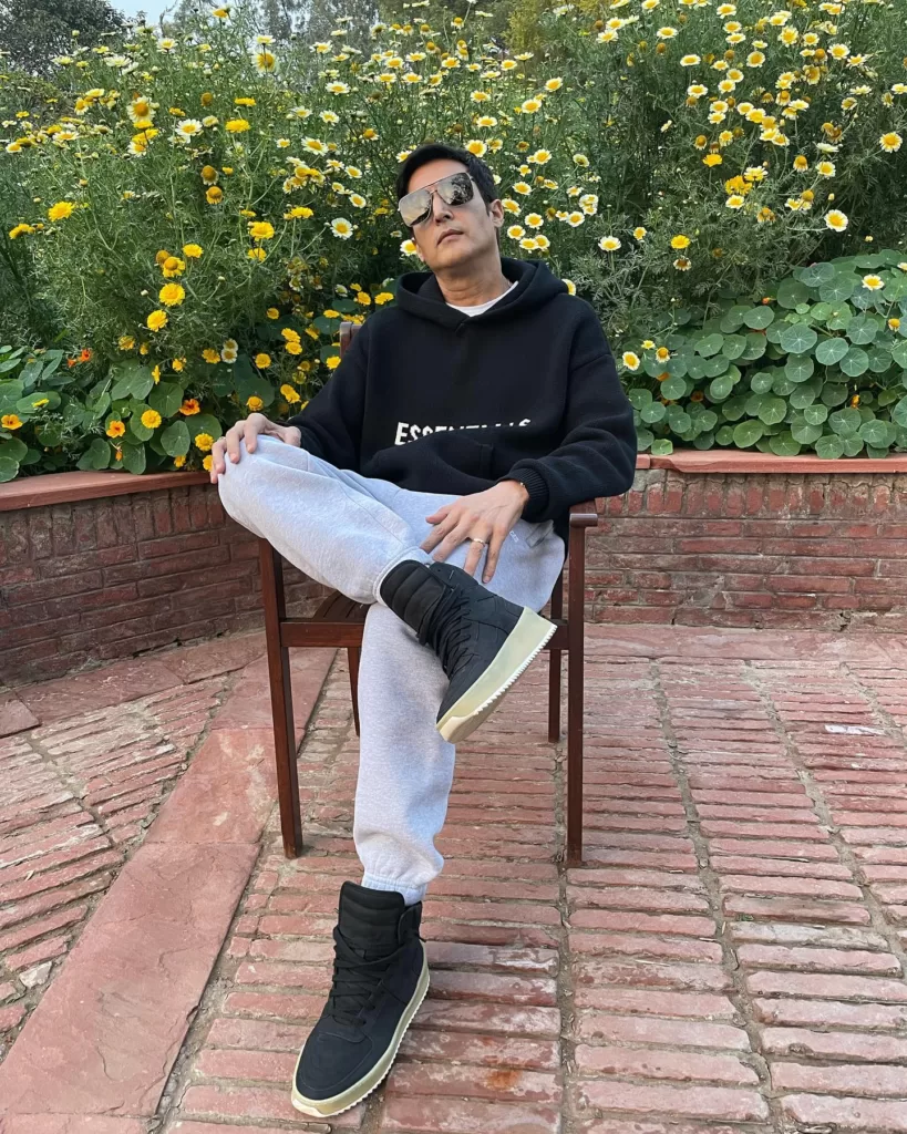 Jimmy Shergill wearing black sweatshirt and shoes with blue jeans.